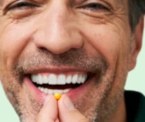 Close up shot of a smiling man about to take one tablet of DulcoLax Tablets in front of a light green background