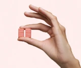 Hand holding two pieces of DulcoLax Soft Chews to show the colour and size, in front of a light pink background