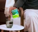 A person holds a box of Dulcolax Overnight Laxative tablets next to a glass of water on a table.