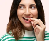 Woman in a striped shirt biting into a striped pink treat, looking to the side.