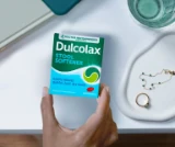 Hand holding Dulcolax Stool Softener box near a glass and jewelry.