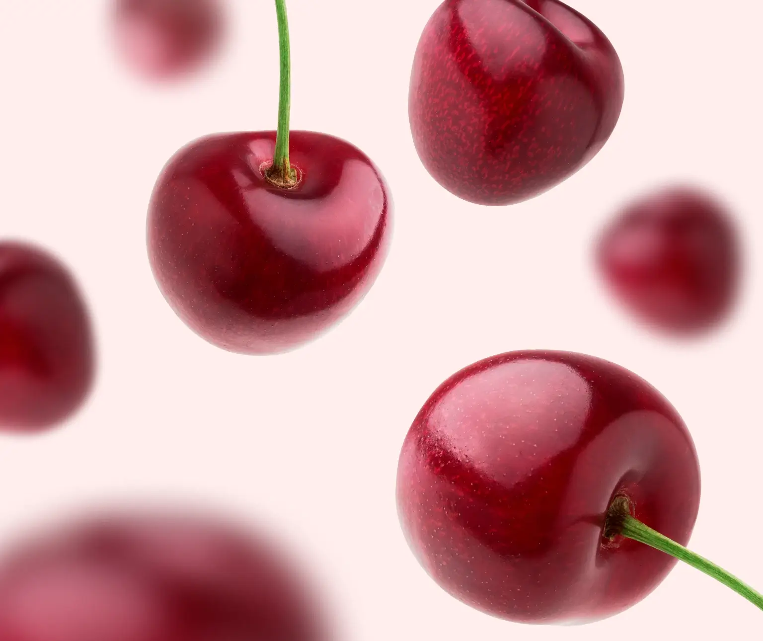 Red cherries with stems arranged on a light pink background.