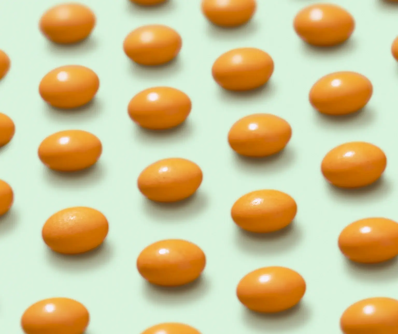 Orange pills arranged in neat rows on a light green background.