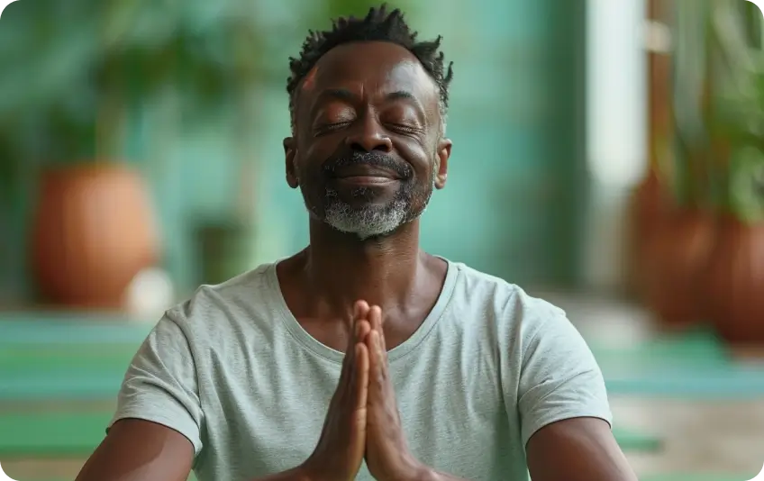 Man meditating with hands in prayer position indoors.