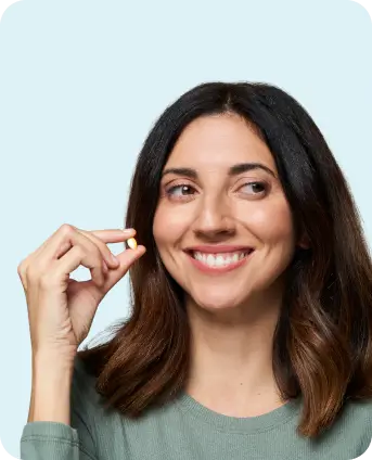 Woman holding a small yellow and white capsule, smiling with a relaxed expression.