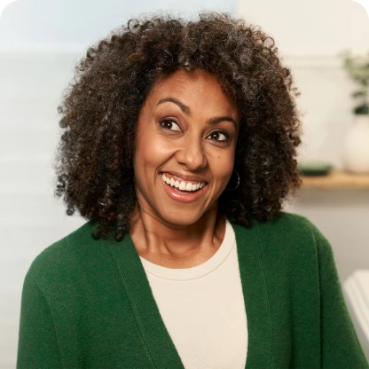 Smiling woman with curly hair wearing a green sweater and earrings.