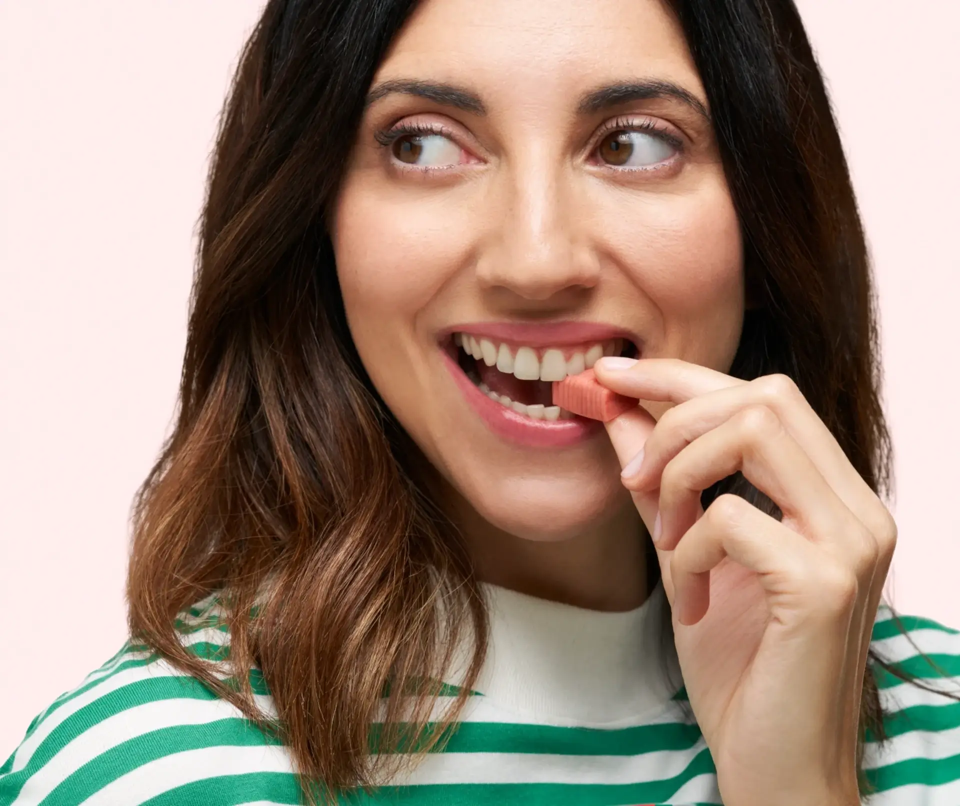 Gros plan d’une femme souriante regardant vers la gauche, sur le point de prendre un morceau de DulcoLax Soft Chews, devant un fond rose pâle