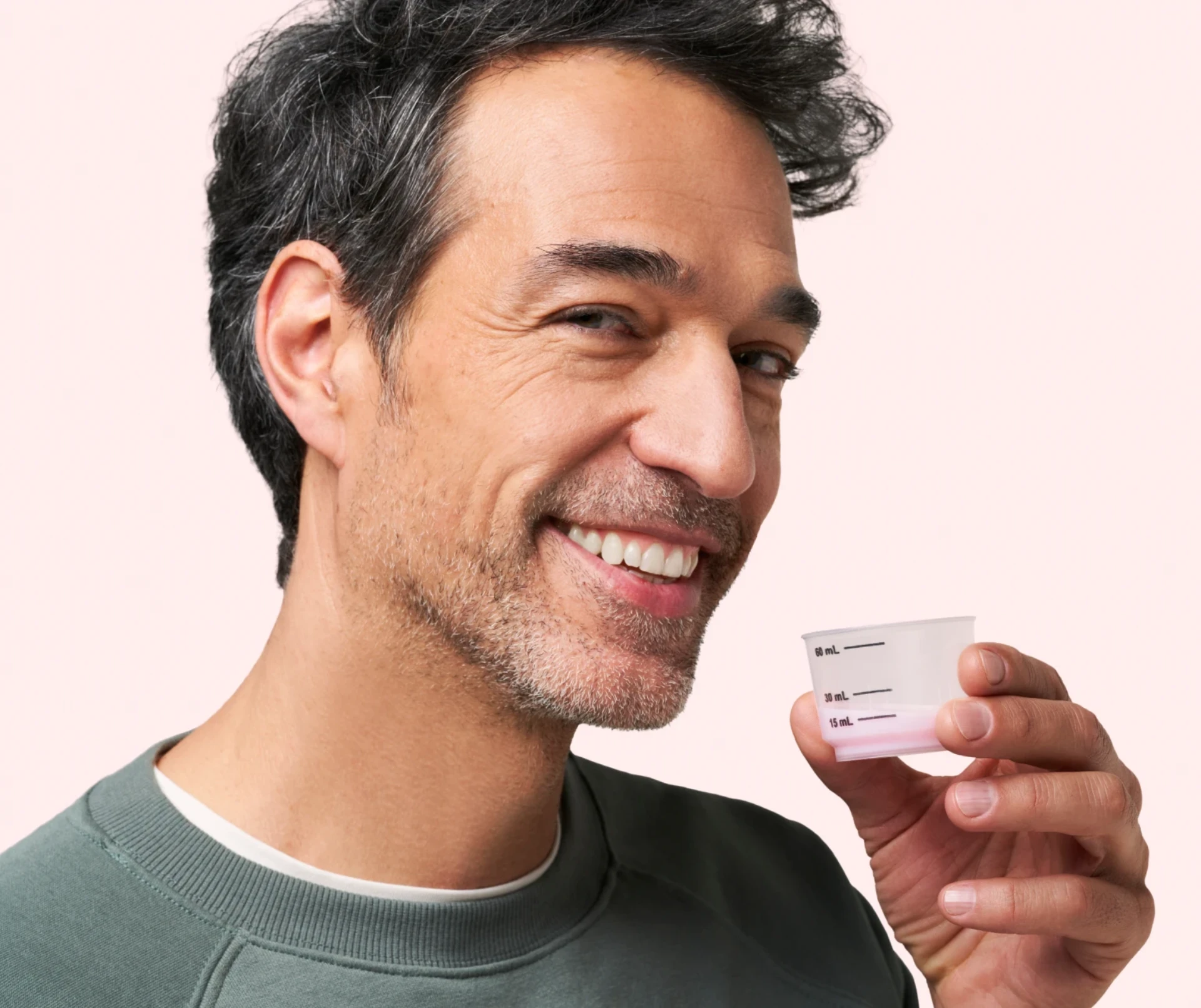Close up shot of a smiling man holding the convenient pre-measured dose cup of DulcoLax Liquid in front of a light pink background