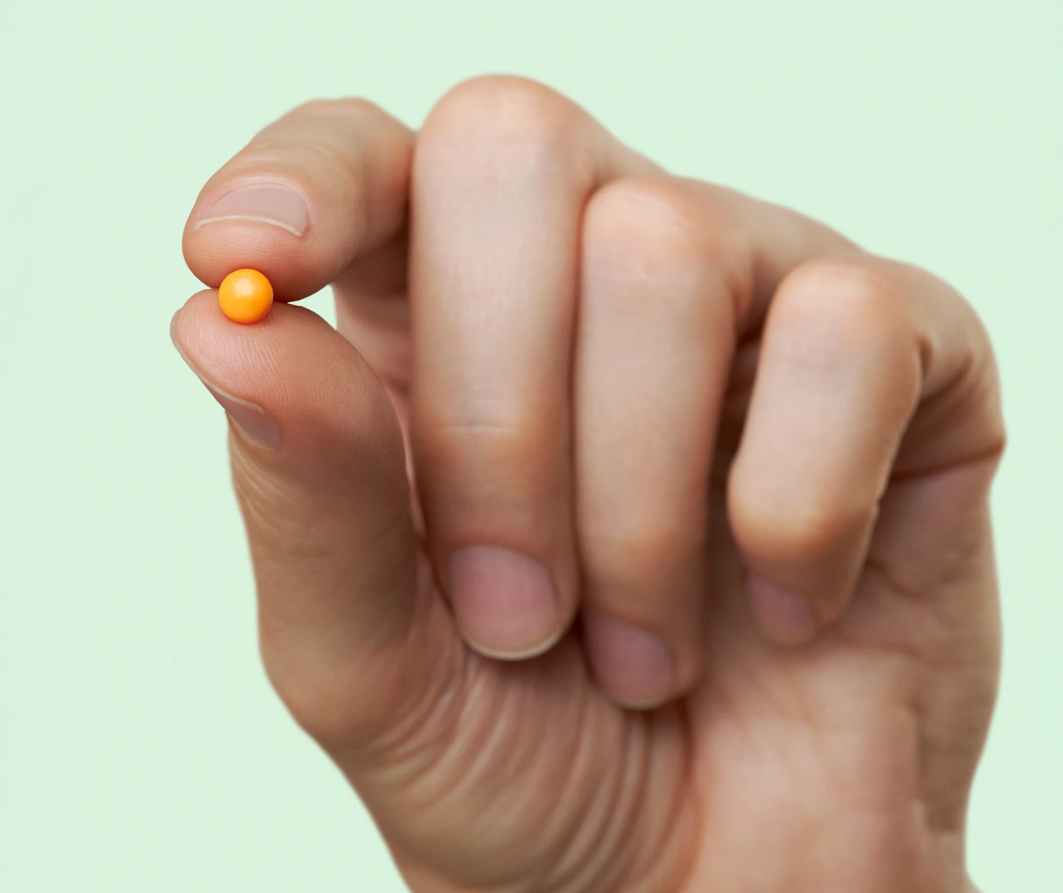 Hand holding one DulcoLax Tablet to show the colour and size, in front of a light green background